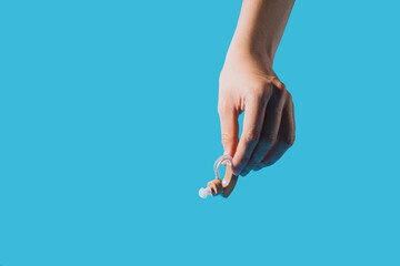 Hearing aid in hand against blue background.