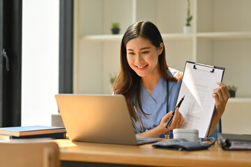 Smiling female doctor having online consultation with patient on laptop in clinic. Tele medical,...