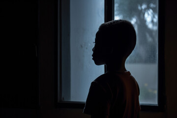 rear view of Lonely african child standing in the dark behind the window looking