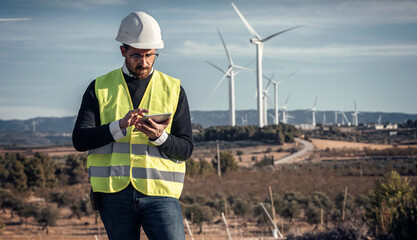 Mature male engineer checking while taking notes with digital tablet of wind turbines operation
