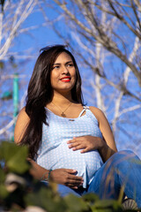 Pregnant young woman sitting on the grass, looking at the horizon and smiling.