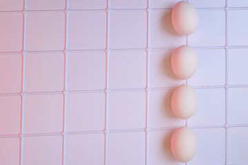 Four fresh chicken eggs on a plastic checkered shelf in pink in refrigerator