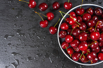 Fresh red ripe sweet cherry with water drops on plate on black slate, stone background. Berry, food background. Top view, banner, header with copy space.