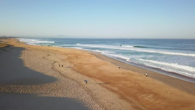 Aerial drone cinematic sunrise early morning waves crashing people walking beachfront Hoosegor Capbreton France Europe Bay of Biscay WSL Quiksilver Pro central Peronze sunny midday forward movement