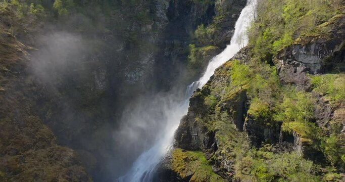 Drone revealing large waterfall rushing down lush green Norway mountain hillside