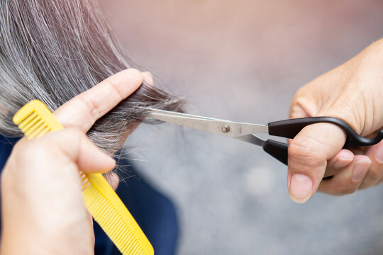 Master cuts gray hair of women at home outdoor, hairdresser makes hairstyle for elder woman.