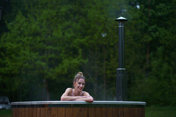 Young happy woman relaxing in hot tub. Enjoying welness SPA outside in the forests. Hot bath SPA