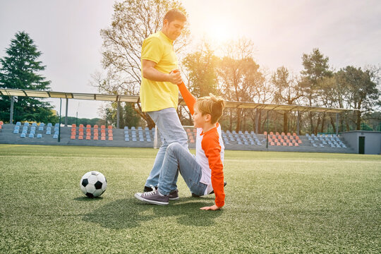 Father and Son play football on stadium, Happy family outdoors, bonding, family fun, players in soccer in dynamic action have fun playing football in sunny day, holidays time.
