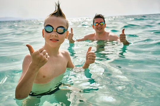 Happy family in swimming goggles, father and son bonding, play, swim in the sea looking at view enjoying summer vacation. Togetherness Friendly concept