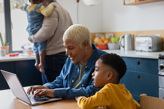 Mom using a laptop with son looking at family in the background