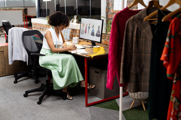 Busy biracial female fashion designer making fashion projects in creative office, unaltered