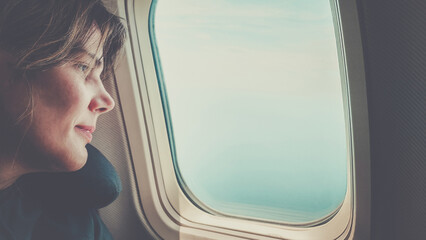 Beautiful girl looks out the window of the airplane. .Summer vacation, travel, melancholy concept.