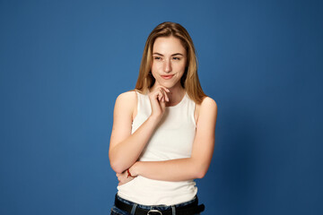 Portrait of young girl, student posing with curious, thoughtful face against blue studio background. Concept of youth, human emotions, facial expression, business, lifestyle, brainstorming