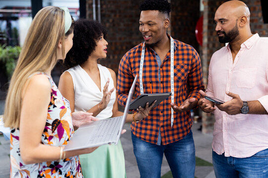 Happy diverse fashion designers using tablets in creative office, unaltered