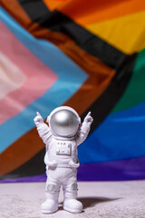 Toy astronaut on Rainbow LGBTQIA flag made from silk material background. Happy pride month. Symbol...