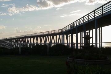 Backlight shot of a long pier over the water and green feilds at sunset