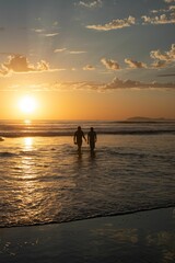 Obraz premium Silhouette view of two people walking out of the water at sunset