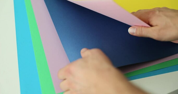 Female designer examines sheets with color gamut samples for home renovation at table. Woman sorts through color options slow motion