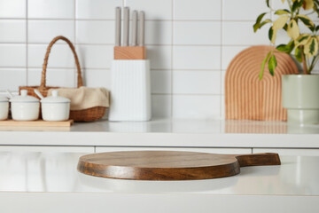 Fototapeta na wymiar Kitchen interior shot with wooden cutting board, knife tray, spice boxes, bamboo basket and a small potted on white tile wall background. Blank space for display products, place your design and text.