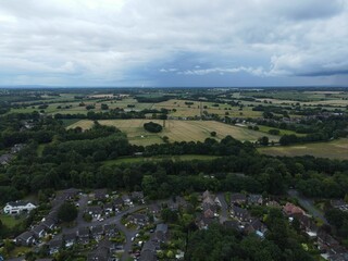Bird's-eye view of a suburban area with the background of woodland and farmland under a cloudy sky
