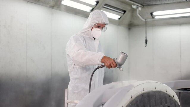 Car painter with mask using spray gun painting car spare parts in painting room, Caucasian worker in protective uniform working in automobile car repair shop, occupations with Chronic pneumonitis risk