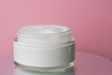 Glass jar with white face cream moisturiser on pink background.