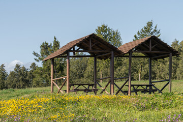 Scenic view of two wooden gazebos in the green field on the background of a forest