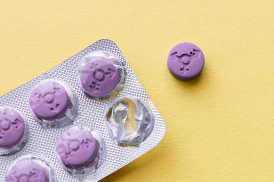 Transgender pills. Hormonal pills. A purple pill with a transgender gender symbol in a blister on a yellow background