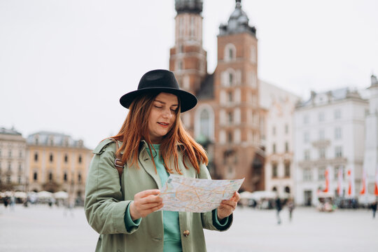 Attractive young female tourist is exploring new city. Redhead girl walking and holding a paper map in Krakow. Traveling Europe in spring. Urban lifestyle banner