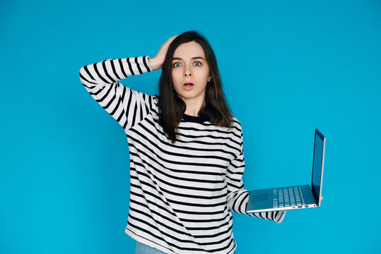 Emotional Young Woman in Striped Sweater Distraught by Bad News on Laptop - Expressive Female Feeling Sad and Disheartened - Isolated Blue Background - Perfect for Conceptual, Emotional