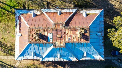 Aerial top view of an old building with a rusty roof in a green field