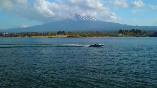 Cinematic aerial view of Mt. Fuij in Japan. Drone flies low over a lake and tilts up to reveal the snow covered top of Mt. Fuij and a speedboat on the lake.