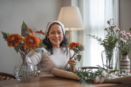 Happy And Attractive Mature Asian Woman Enjoying With Her Online Flower Arrangement Workshop At Home.