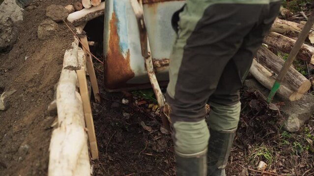 Gardener Dumping Dried Leaves Using Wheelbarrow Into Compost Pit  For Growing Plants And Crops. - high angle