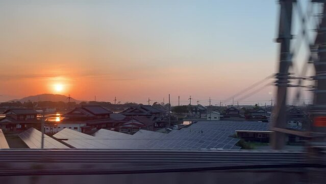 Radiant sunset from the window of a high-speed bullet train in Japan, revealing striking silhouettes of houses and landscapes during dusk.