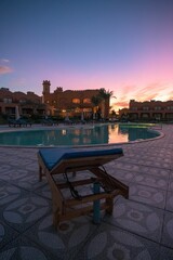 Vertical of a blue poolside lounge chair next to a big swimming pool captured at sunset