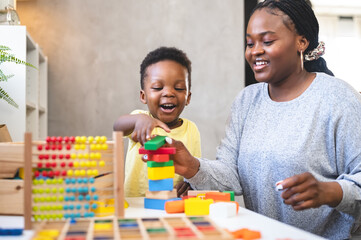 A cute little African child plays with colorful didactic educational toys. His proud mother supports him. Kindergarten teacher with child. - obrazy, fototapety, plakaty