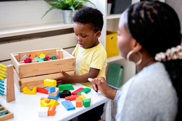 A cute little African child plays with colorful didactic educational toys. His proud mother...