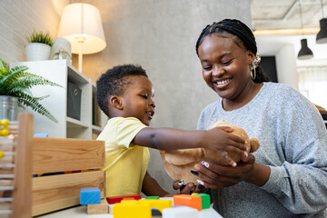 A cute little African child plays with colorful didactic educational toys. His proud mother supports him. Kindergarten teacher with child. - obrazy, fototapety, plakaty