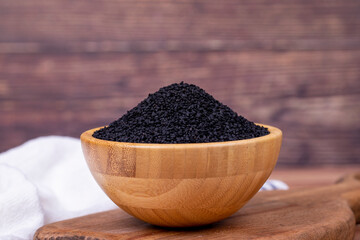 Black cumin or nigella sativa on wooden background. Black cumin seeds in wooden bowl. Kalonji, nigella, black cumin