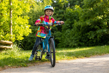 Happy kid boy, having fun in park with a bicycle on beautiful day. Active child wearing bike helmet