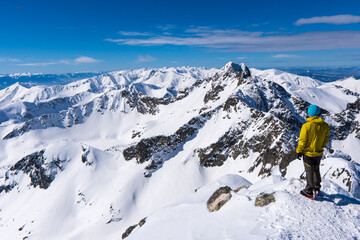 A Tourist standing on a mountain top above the clouds and looking at the view. Direct sunlight. Clear blue sky. Winter. Mountaineering. High Tatras mountain in Poland and Slovakia