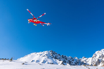 Fototapeta na wymiar Red rescue helicopter moving in blue sky with blur propeller in winter mountains. Europe slovakia poland