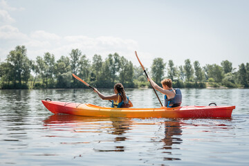 side view of active multiethnic couple in life vests holding paddles while sailing in sportive...
