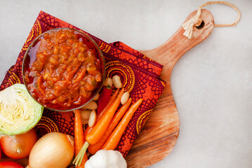 Traditional South African Chakalaka, a popular spicy side dish or relish. On a wooden board with fresh ingredients and traditional South African printed fabric known as Shwe Shwe