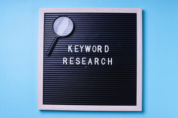 Keyword Research written on the letter board with magnifying glass on blue background. SEO concept