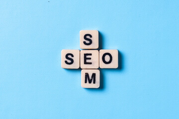 Wooden cubes with the word SEO and SEM isolated on blue background. Search Engine Marketing and...