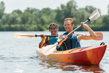 active redhead man and charming african american woman in life vests spending time on river while...