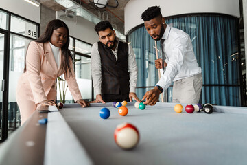Young multiracial people in suits playing pool at office lobby