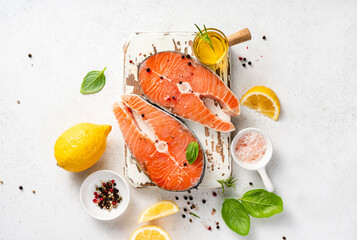 Fresh raw salmon steaks with spices, lemons and pink salt on white wooden board. Top view of fish...